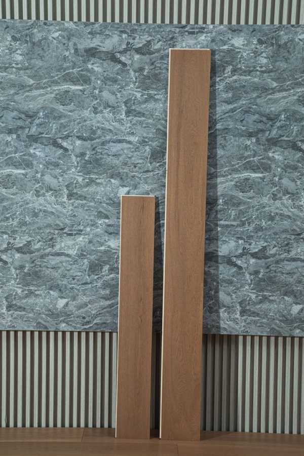 Two planks of QH9906 Walnut Floorboards leaning against a textured wall.